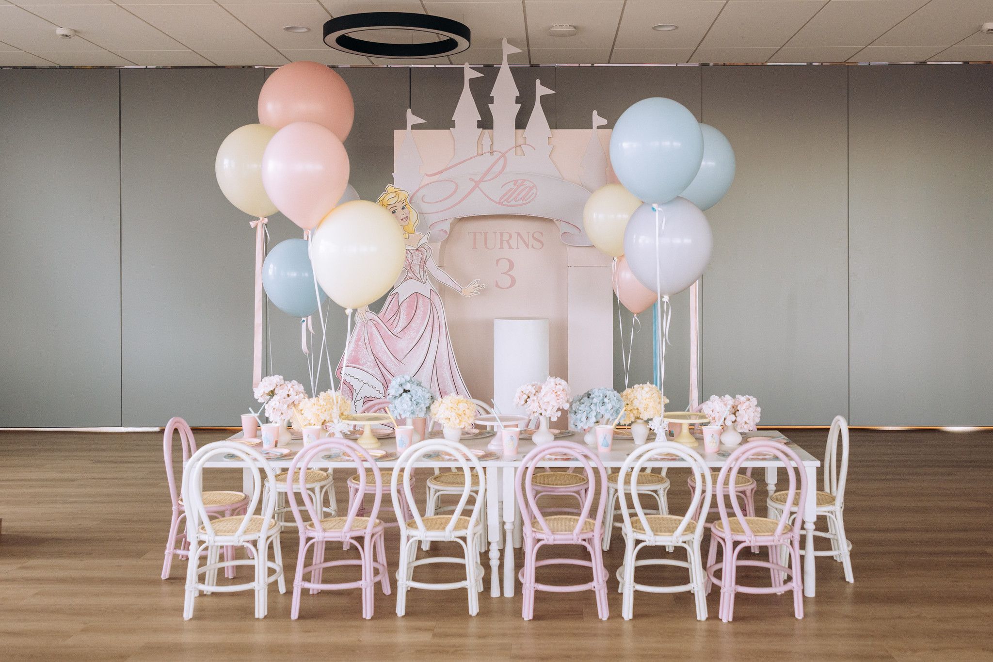 Tematska dekoracija dječjeg rođendana u stilu princeza s pastelno ružičastim dvorcem, ilustracijom princeze i helij balonima u pastelnim bojama bojama.
